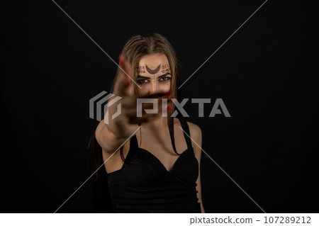 The witch extends her hand to the camera from the twilight inviting you to the Halloween holiday. On a black background, a beautiful female witch with long hair calls you to Halloween. 107289212