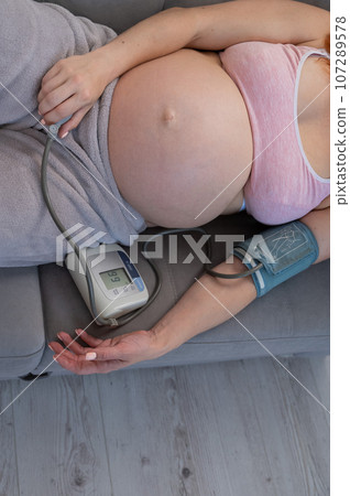Close-up of the belly of a pregnant woman measuring blood pressure with a tonometer. Close-up of the belly of a pregnant woman measuring blood pressure with a tonometer. 107289578