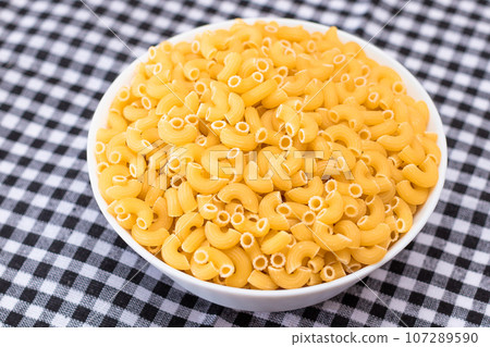 Uncooked Chifferi Rigati Pasta in White Cup on Black Checkered Towel 107289590