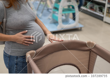 Caucasian pregnant woman chooses a playpen crib in a children's store.  107289735