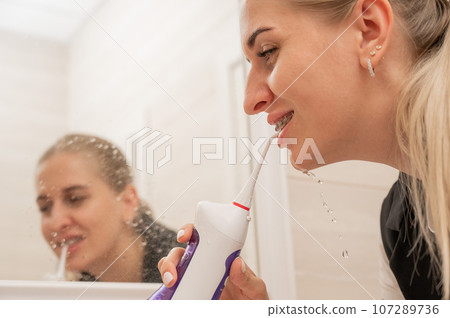 A woman with braces on her teeth uses an irrigator. Close-up portrait.  107289736