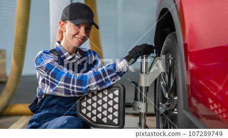 A female auto mechanic makes a camber. Woman working in a car service. A female auto mechanic makes a camber. Woman working in a car service. 107289749