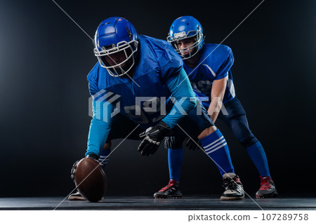 Two American football players are ready to start the game on a black background.  107289758