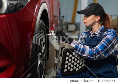 A female auto mechanic makes a camber. Woman working in a car service. A female auto mechanic makes a camber. Woman working in a car service. 107289874