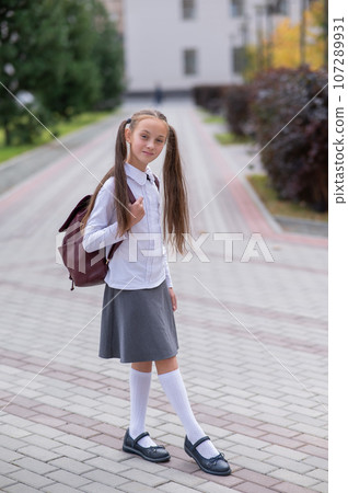 Caucasian girl in uniform and with a backpack goes from school.  107289931