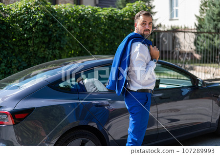 Attractive bearded man in a blue suit near a black car in the countryside in summer. Attractive bearded man in a blue suit near a black car in the countryside in summer. 107289993