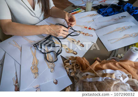 Faceless woman draws underwear sketches. Close-up of fashion designer's hands with lace bra. Faceless woman draws underwear sketches. Close-up of fashion designer's hands with lace bra. 107290032