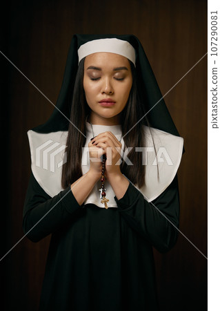 Portrait of religious nun praying with eyes closed holding crucifix rosary Portrait of religious nun praying with eyes closed holding crucifix rosary 107290081
