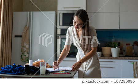 Woman drawing sketches of swimwear and underwear in watercolor while sitting in the kitchen.  107290090