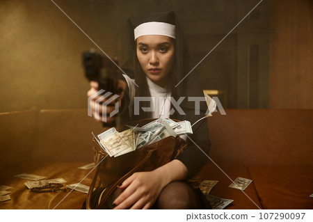 Confident woman in nun robe and headdress aiming handgun 107290097