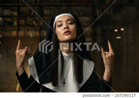 Portrait of passionate catholic nun gesturing rock symbol with hands Portrait of passionate catholic nun gesturing rock symbol with hands 107290117