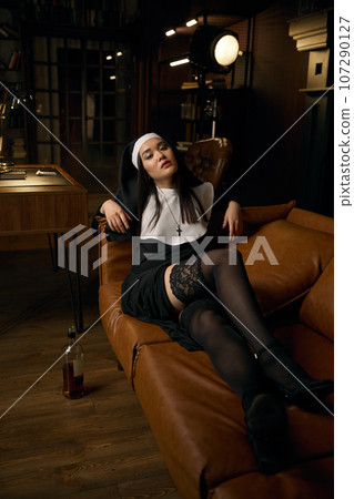 Beautiful striptease dancer dressed as nun lying on leather sofa Beautiful striptease dancer dressed as nun lying on leather sofa 107290127