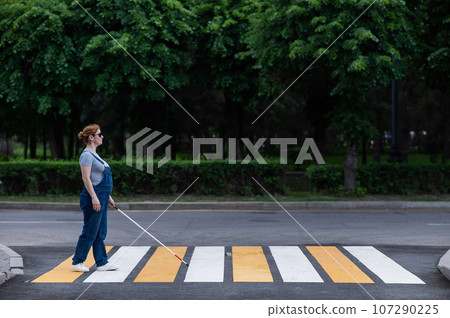 Blind pregnant woman crosses the road at a crosswalk with a cane. Blind pregnant woman crosses the road at a crosswalk with a cane. 107290225