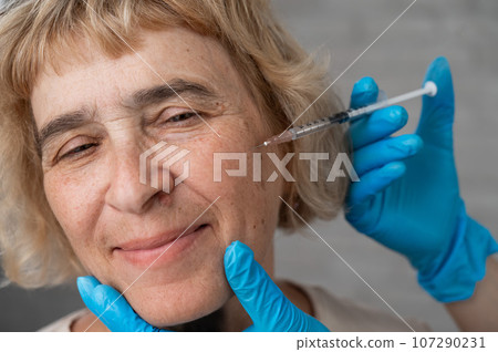 Doctor makes beauty injections in the face of an old caucasian woman. Doctor makes beauty injections in the face of an old caucasian woman. 107290231