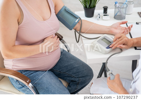 The doctor measures the pressure of a pregnant woman. The doctor measures the pressure of a pregnant woman. 107290237