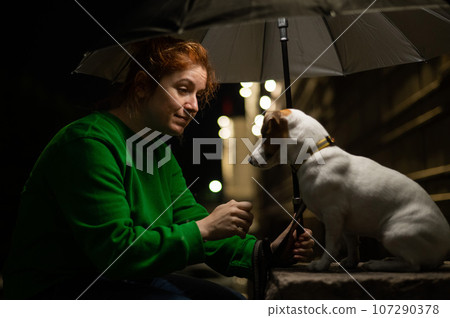 Red-haired woman and dog jack russell terrier under an umbrella in the dark. Red-haired woman and dog jack russell terrier under an umbrella in the dark. 107290378