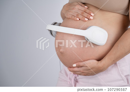 A pregnant woman holds headphones against her bare tummy. The expectant mother lets her child listen to music.  107290387