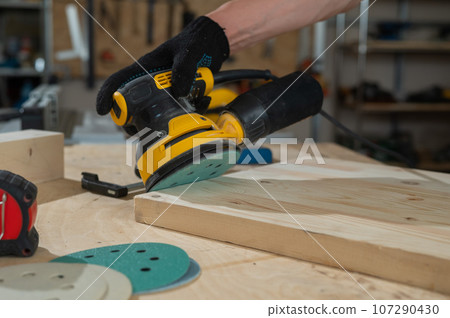 A man using an orbital wood sander in a workshop. Close-up of a carpenter's hands. 107290430