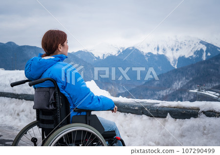 Rear view of a woman in a wheelchair travels in the mountains in winter. Rear view of a woman in a wheelchair travels in the mountains in winter. 107290499
