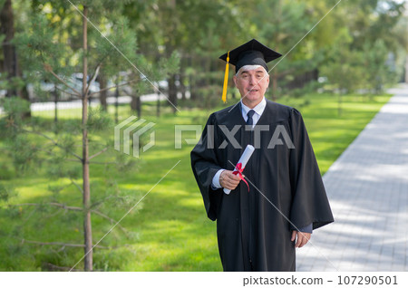 Serious old man in graduation gown holding diploma outdoors. Serious old man in graduation gown holding diploma outdoors. 107290501