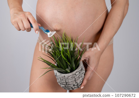 A faceless pregnant woman shaves a plant with a razor. Metaphor for epilation of the bikini area.  107290672