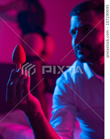 Bearded caucasian man holding an anal plug. Close-up of female buttocks in underwear. Sexual preferences of the couple. Bearded caucasian man holding an anal plug. Close-up of female buttocks in underwear. Sexual preferences of the couple. 107290695