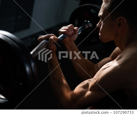 Man doing EZ barbell bicep exercises on Scott bench. Man doing EZ barbell bicep exercises on Scott bench. 107290733