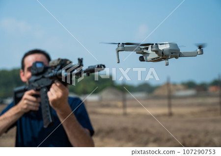 Man aiming to shoot a rifle at a flying drone outdoors.  107290753