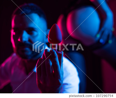 Bearded caucasian man holding an anal plug. Close-up of female buttocks in underwear. Sexual preferences of the couple. Bearded caucasian man holding an anal plug. Close-up of female buttocks in underwear. Sexual preferences of the couple. 107290754