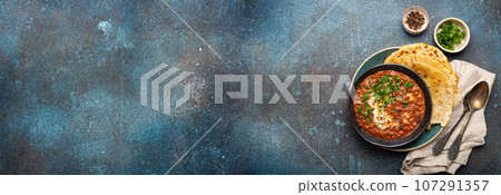 Traditional Indian Punjabi dish Dal makhani with lentils and beans in black bowl served with naan flat bread, fresh cilantro and two spoons on blue concrete rustic table top view. Space for text 107291357