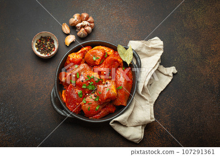 Raw uncooked chopped pieces of meat marinated with seasonings and parsley in black casserole dish top view on dark rustic background. Cooking ragout stew with marinated meat fillet pieces 107291361