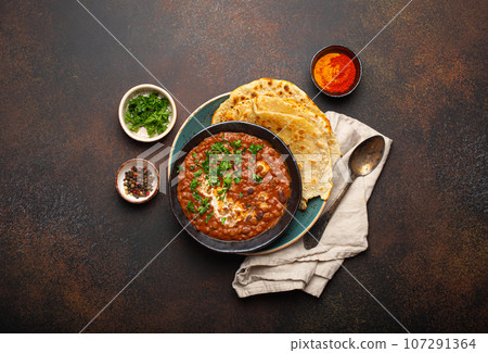 Traditional Indian Punjabi dish Dal makhani with lentils and beans in black bowl served with naan flat bread, fresh cilantro and two spoons on brown concrete rustic table top view Traditional Indian Punjabi dish Dal makhani with lentils and beans in black bowl served with naan flat bread, fresh cilantro and two spoons on brown concrete rustic table top view 107291364