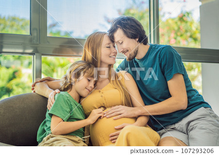Expectant parents, mom, dad, and their eldest son share a heartwarming moment on the sofa, discussing the exciting journey of pregnancy 107293206
