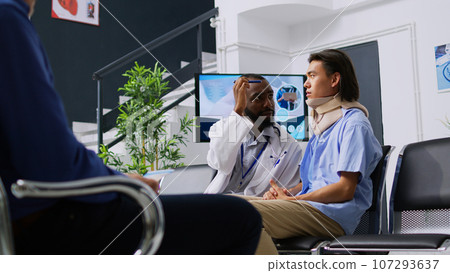 African american medic checking patient vision after medical surgery in hospital waiting room. Asian man wearing cervical neck collar discussing health care treatment with physician doctor African american medic checking patient vision after medical surgery in hospital waiting room. Asian man wearing cervical neck collar discussing health care treatment with physician doctor 107293637