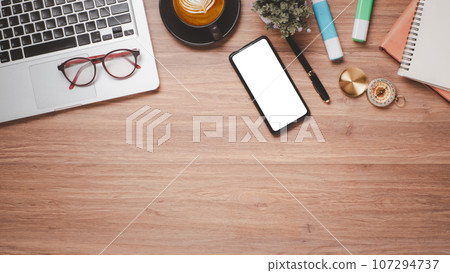 Wooden desk workplace with blank screen smartphone for product display, laptop, eyeglass, notebook, pen and cup of coffee, Top view flat lay with copy space. 107294737