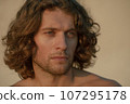 Close-up of young adult handsome man with long curly hair and stubble intently looks forward outdoor 4K 107295178
