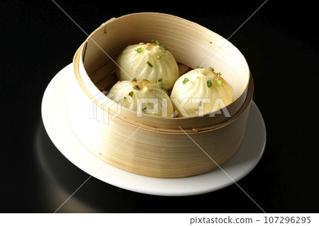 Xiaolongbao steamed in a steamer basket photographed against a black background 107296295