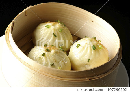 Xiaolongbao steamed in a steamer basket photographed against a black background 107296302