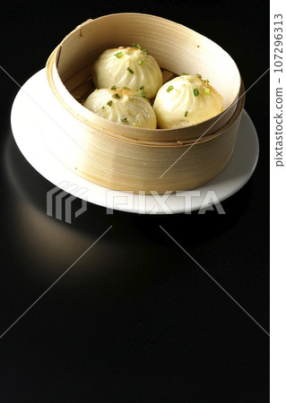 Xiaolongbao steamed in a steamer basket photographed against a black background 107296313