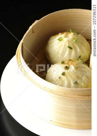 Xiaolongbao steamed in a steamer basket photographed against a black background 107296315