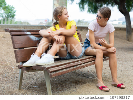 Two friendly young girls sitting on bench Two friendly young girls sitting on bench 107298217
