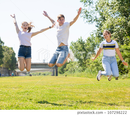 Cheerful teenage girls and guy jumping in summer park 107298222