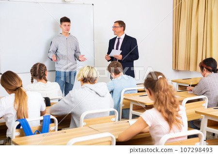 Positive schoolboy is standing near whiteboard and answer about task in classroom 107298493
