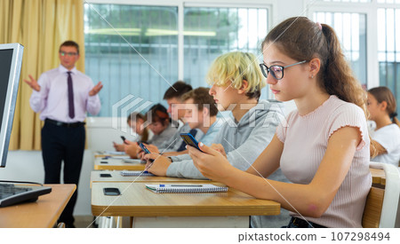 Schoolchildren with mobile phones in informatics lesson 107298494