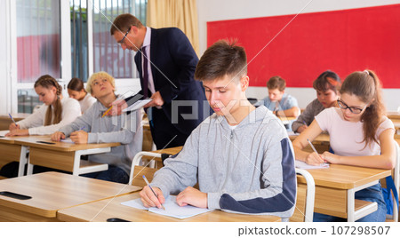 Teacher man helping students during lesson in schoolroom 107298507