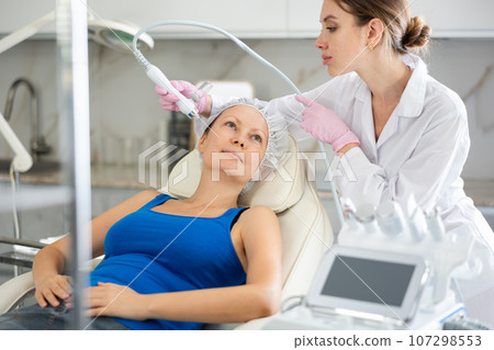 Beautiful female doctor making facial gas-liquid oxygen water epidermal peeling using macromolecule atomizing pen for adult woman at beauty salon. Skin care concept. Beauty treatment 107298553