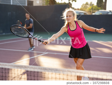 Young woman in skirt playing tennis on court 107298608