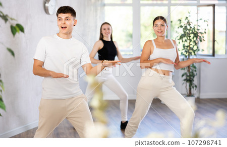 Guy and young girls in good mood actively move and dance reggaeton at choreography lesson 107298741
