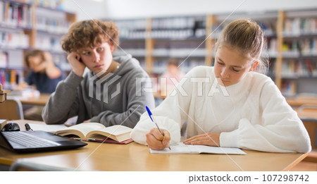 Schoolgirl and schoolboy are sitting together at the same desk at a lesson in school class Schoolgirl and schoolboy are sitting together at the same desk at a lesson in school class 107298742
