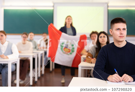 Teenage students in class and listening carefully to female teacher holding Peru flag in hands Teenage students in class and listening carefully to female teacher holding Peru flag in hands 107298820